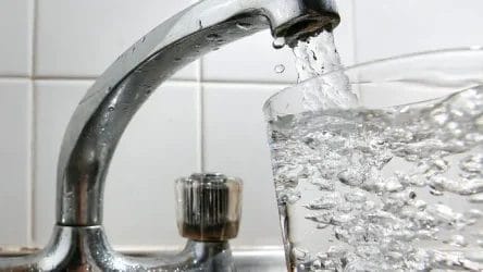 A glass is being filled with water from a running kitchen tap, with clear bubbles visible in the water.