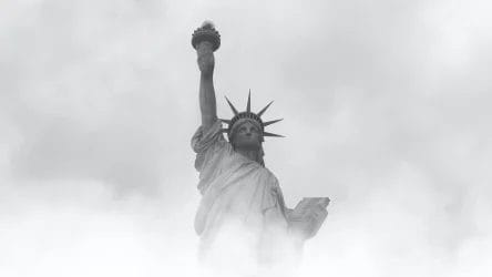 The Statue of Liberty is partially obscured by fog or clouds, with its torch and face visible against a grey sky.