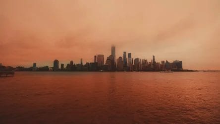 The image shows a city skyline across a body of water under an orange sky, with some skyscrapers partially obscured by haze or fog.